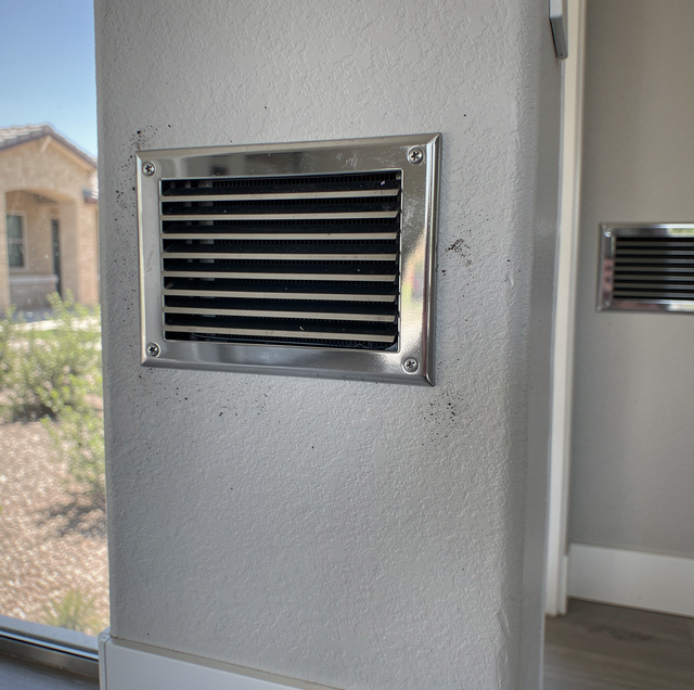 Metal vent with horizontal slats mounted on white textured wall of building exterior.