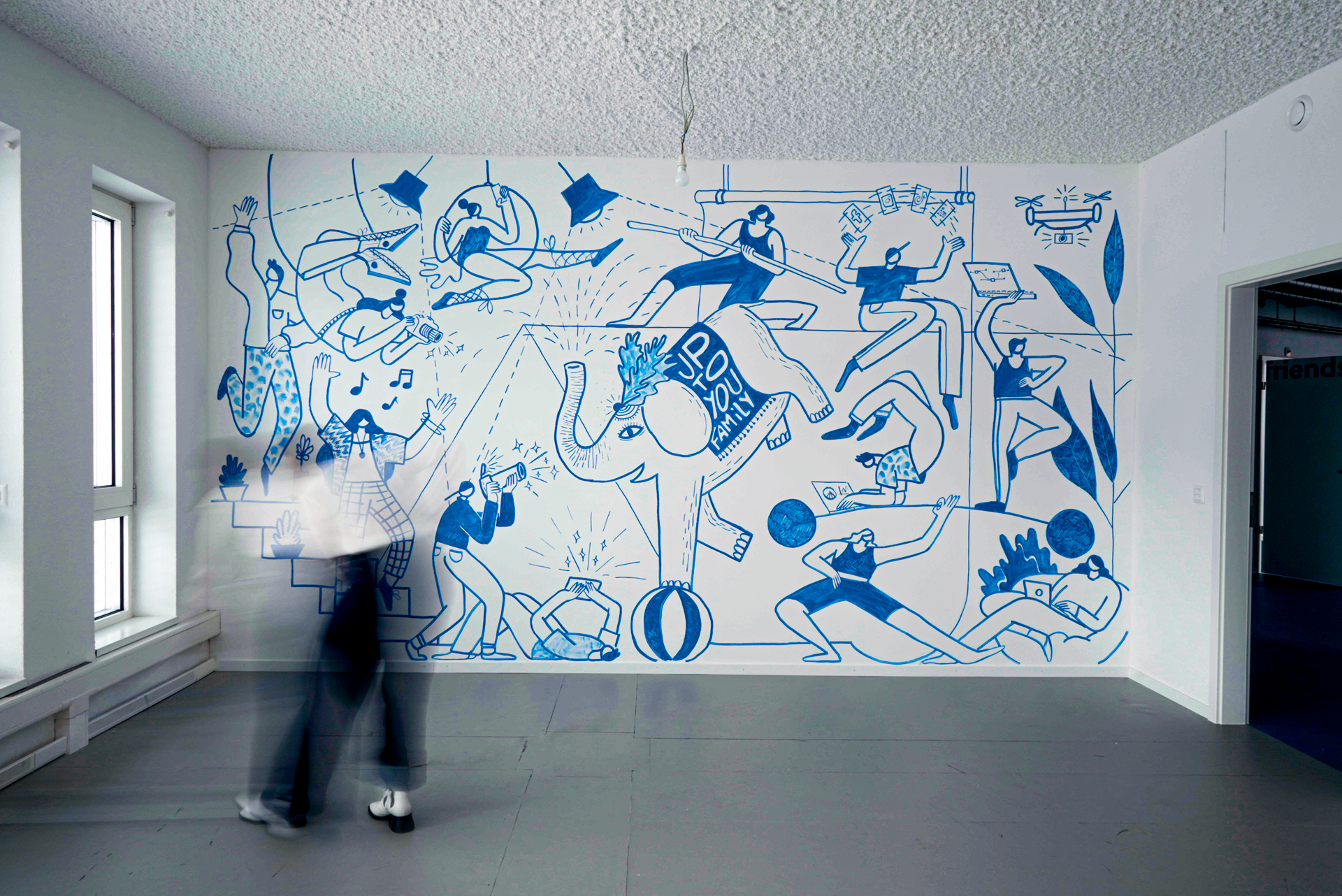 Mur peints avec scène de dessins bleus d'enfants jouant avec un éléphant portant un panneau 'Support Your Family', et d'autres enfants faisant du sport et utilisant des appareils électroniques, dans une pièce avec fenêtres et porte.