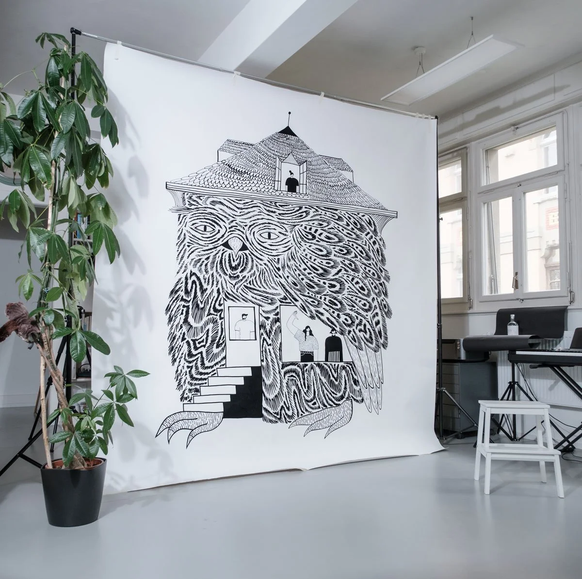 Un grand fresque sur papier en noir et blanc représentant un hibou aux détails stylisés, avec des petits personnages dessinés à l'intérieur de l'oiseau.