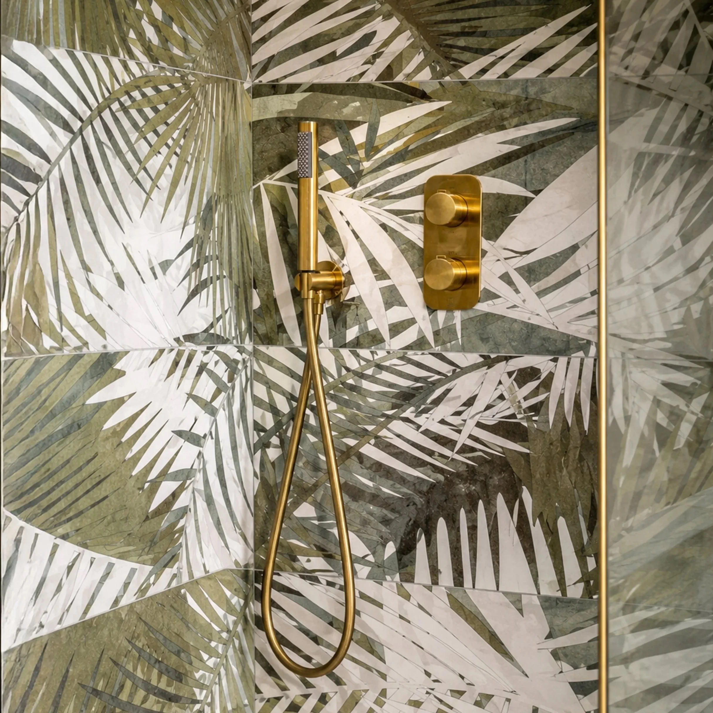 A decorative shower wall with large leaf patterns and gold fixtures, including a showerhead and control knobs.
