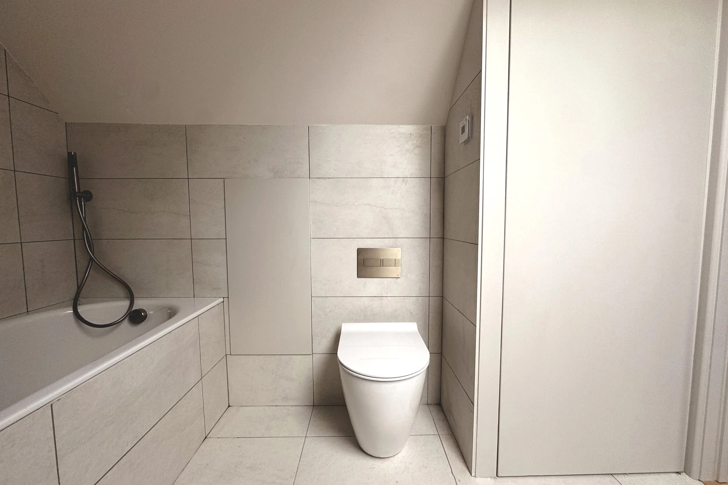 A beautiful minimalist bathroom in East Peckham with integrated storage, grey panelling, bath with brushed brass fixtures, shower and white toilet