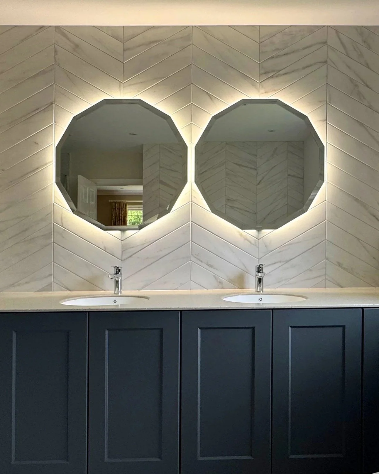 A modern bathroom with two round mirrors featuring backlit LED lighting, two sinks, and a navy blue vanity cabinet.