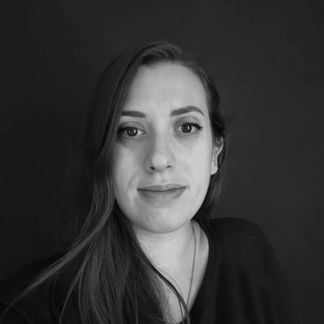Black and white portrait of a woman with long hair, looking directly at the camera with a neutral expression, against a dark background.