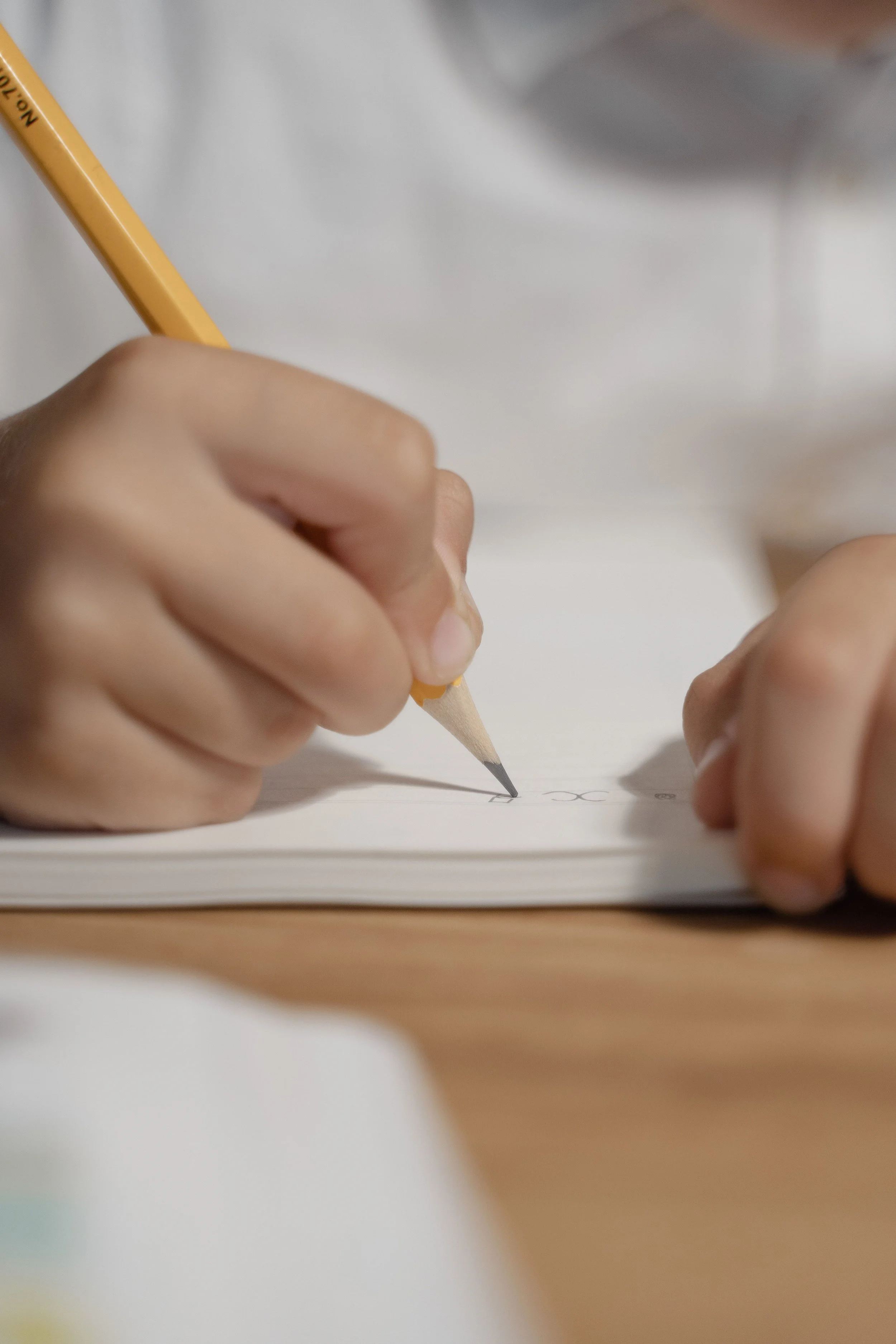 Close-up of a person writing on paper with a yellow pencil.