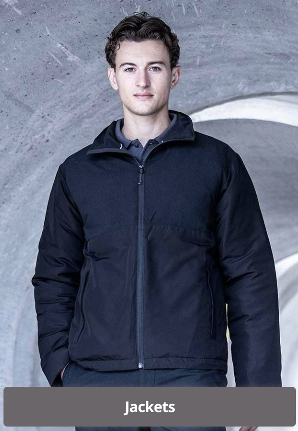 A young man with curly brown hair wearing a black jacket standing in front of a concrete tunnel.