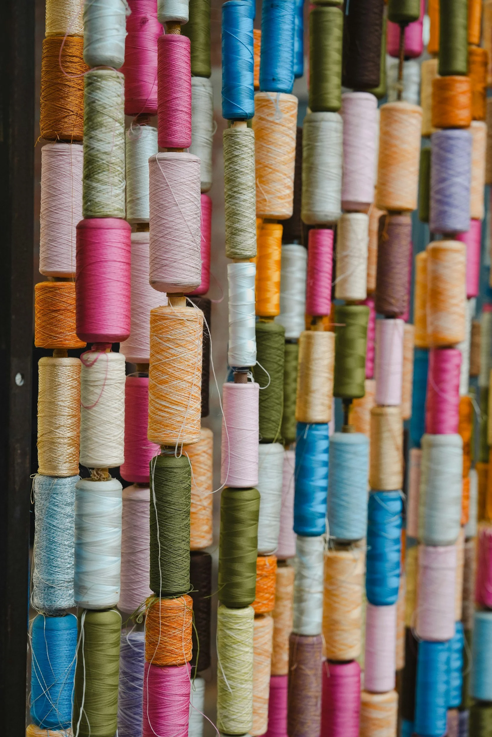 Multiple spools of colored thread hanging on a wall in a shop or a textile workshop.