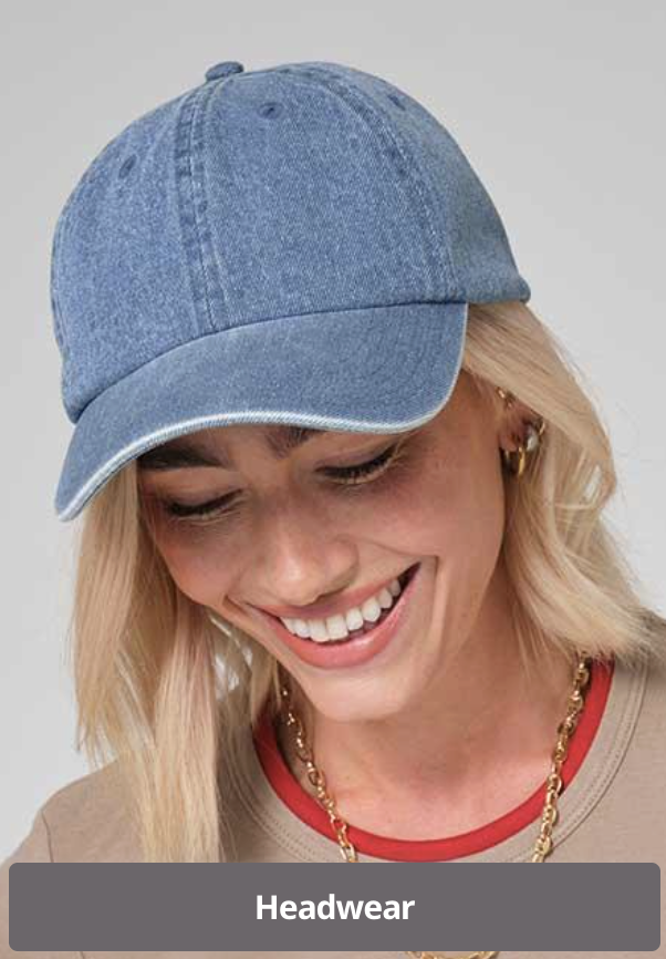 A woman wearing a light blue denim baseball cap, smiling and looking down, with blonde hair and gold jewelry.
