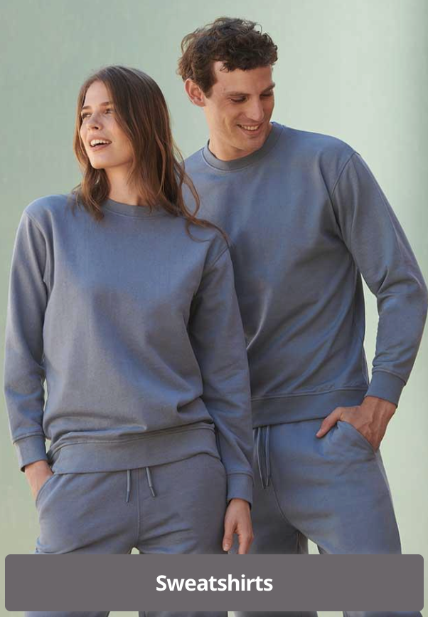 A man and woman standing side by side, both wearing matching blue sweatshirts and sweatpants, smiling and looking at each other.