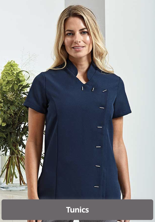 A woman with blond hair in a blue tunic, standing indoors near a plant with green leaves.
