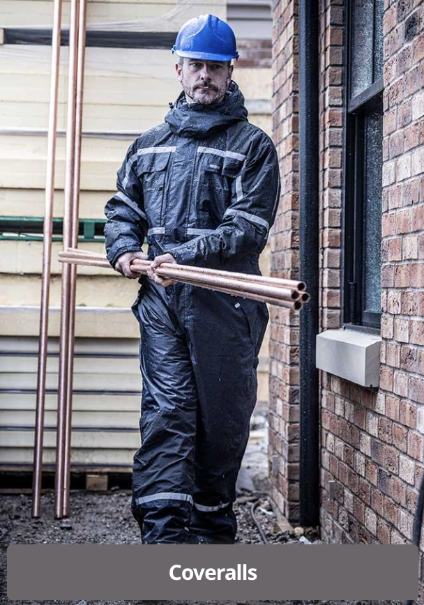 Construction worker wearing a blue hard hat and waterproof coveralls holding copper pipes at a construction site.