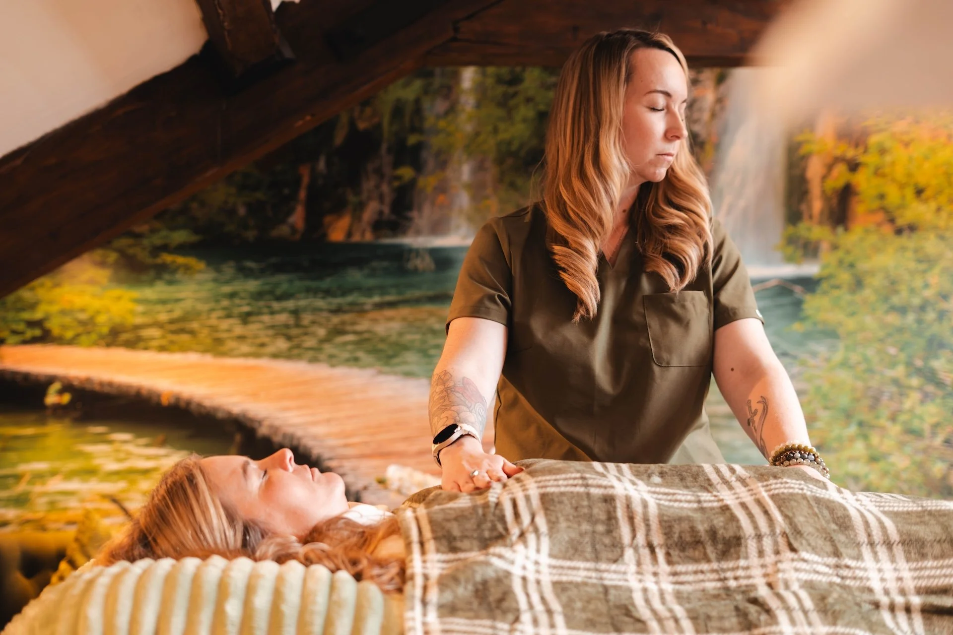 A woman receiving a massage while lying on a table, with a scenic nature mural in the background.