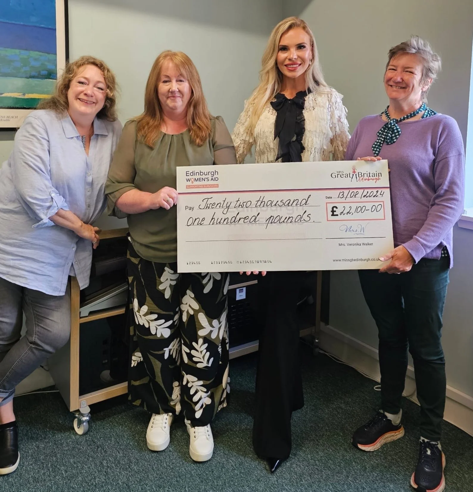Four women standing together, holding a large check for 22,100 pounds, presented to Edinburgh Women's Aid.