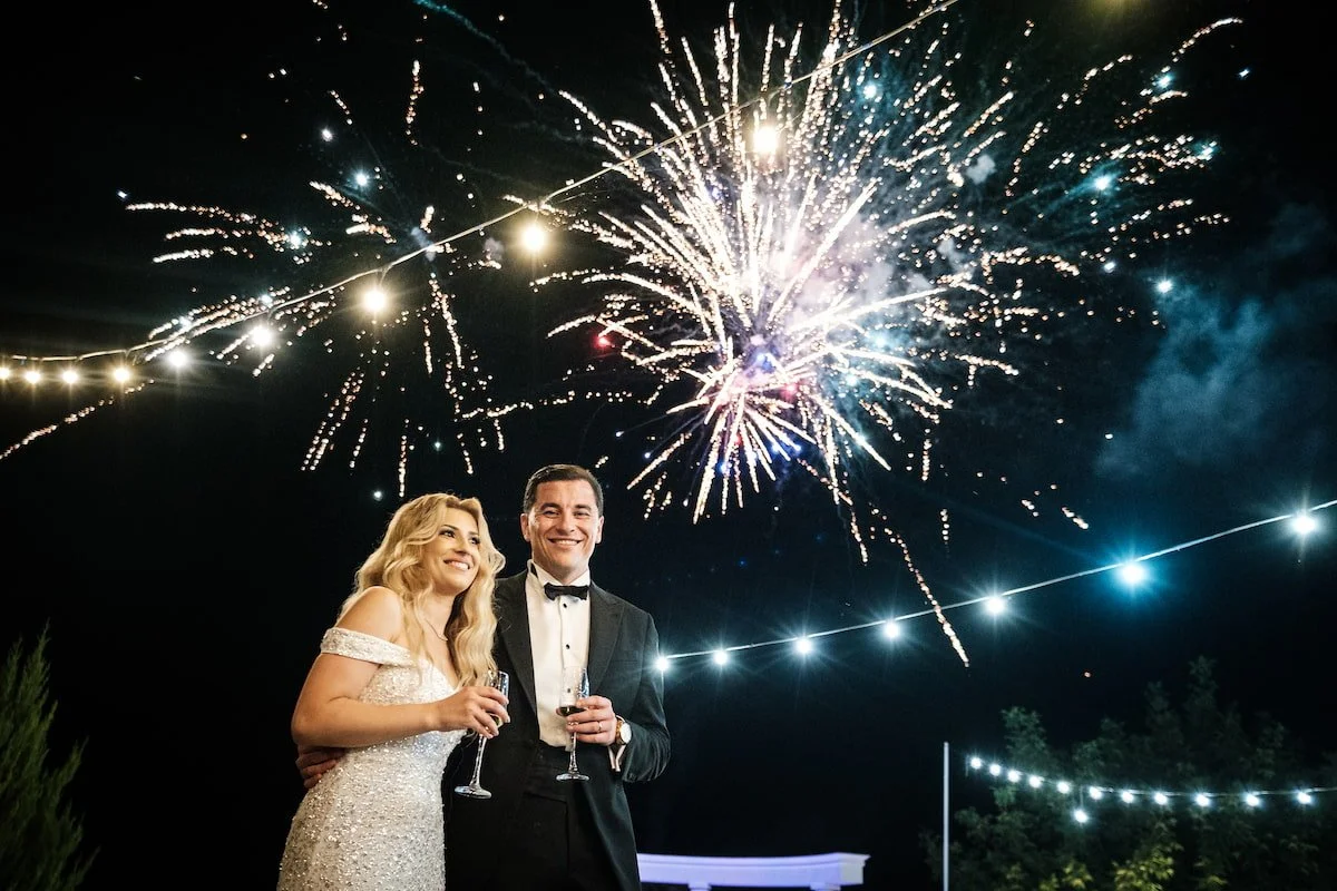 Bride and groom celebrating under fireworks and string lights during an elegant evening wedding reception.