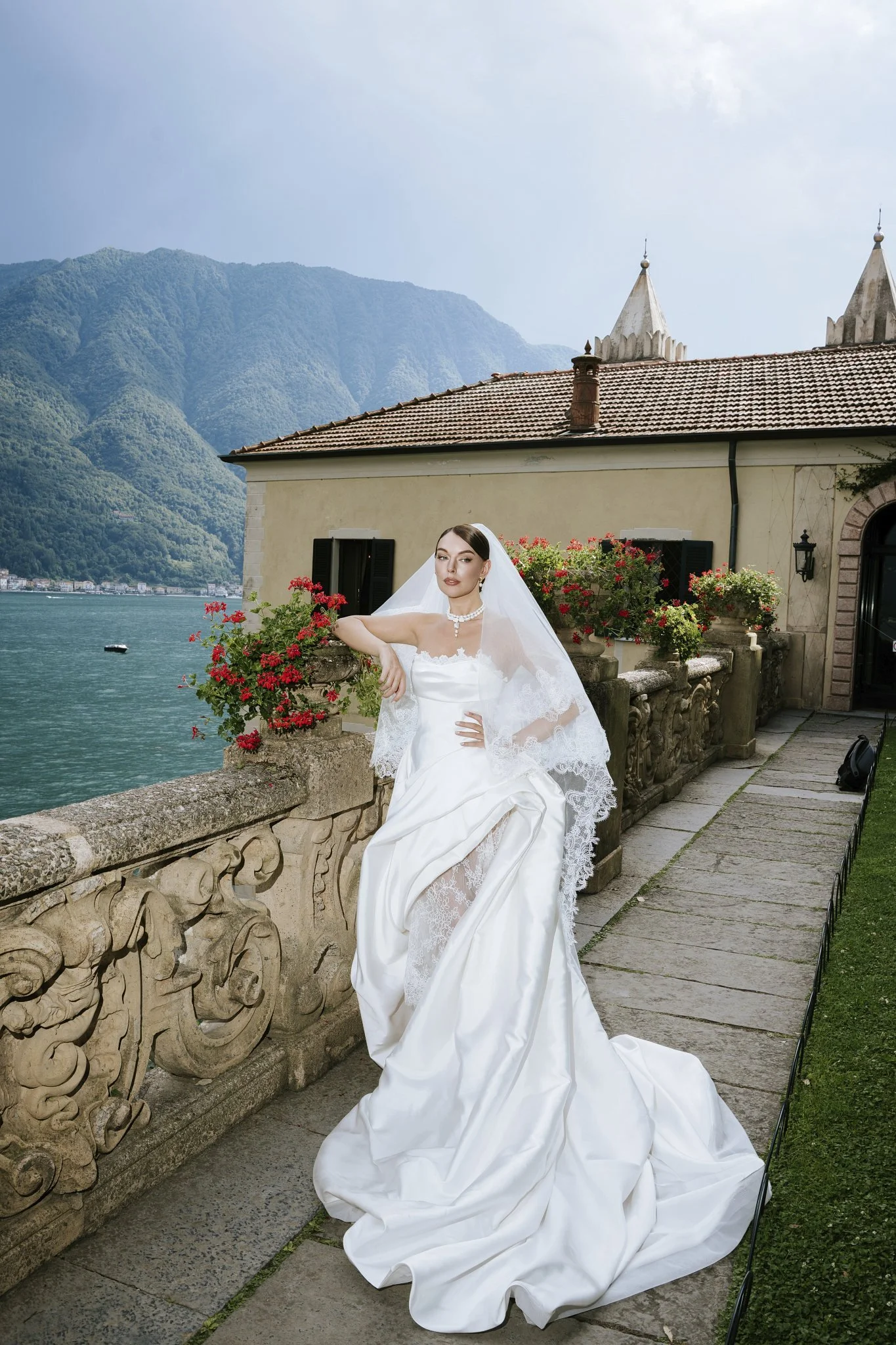 Bride in a veil on the stone balcony at Villa del Balbianello, Lake Como, with the water and mountains behind her.