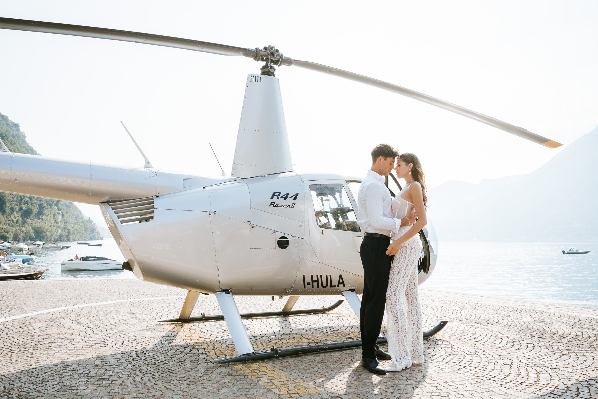 Bride and groom standing beside a white helicopter on Lake Como during a luxury destination wedding.