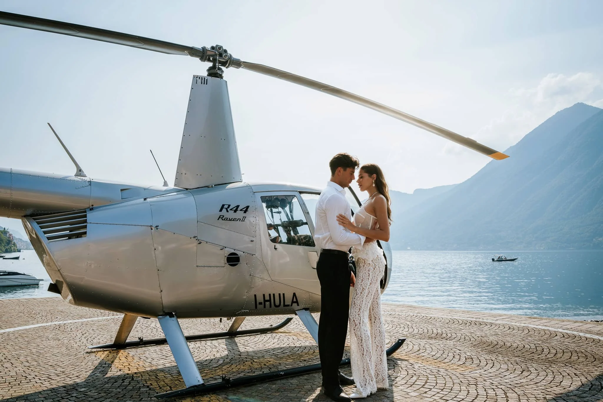 Bride and groom standing beside a white helicopter on Lake Como during a luxury destination wedding.
