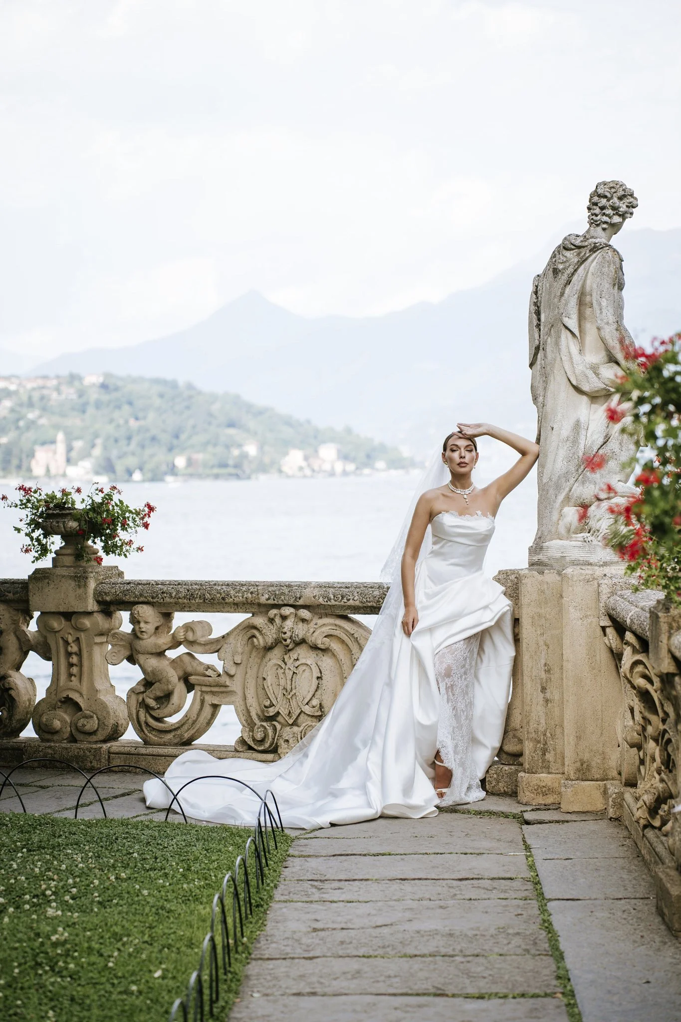 Bride in a white wedding dress on the stone loggia at Villa del Balbianello, overlooking Lake Como and the mountains.