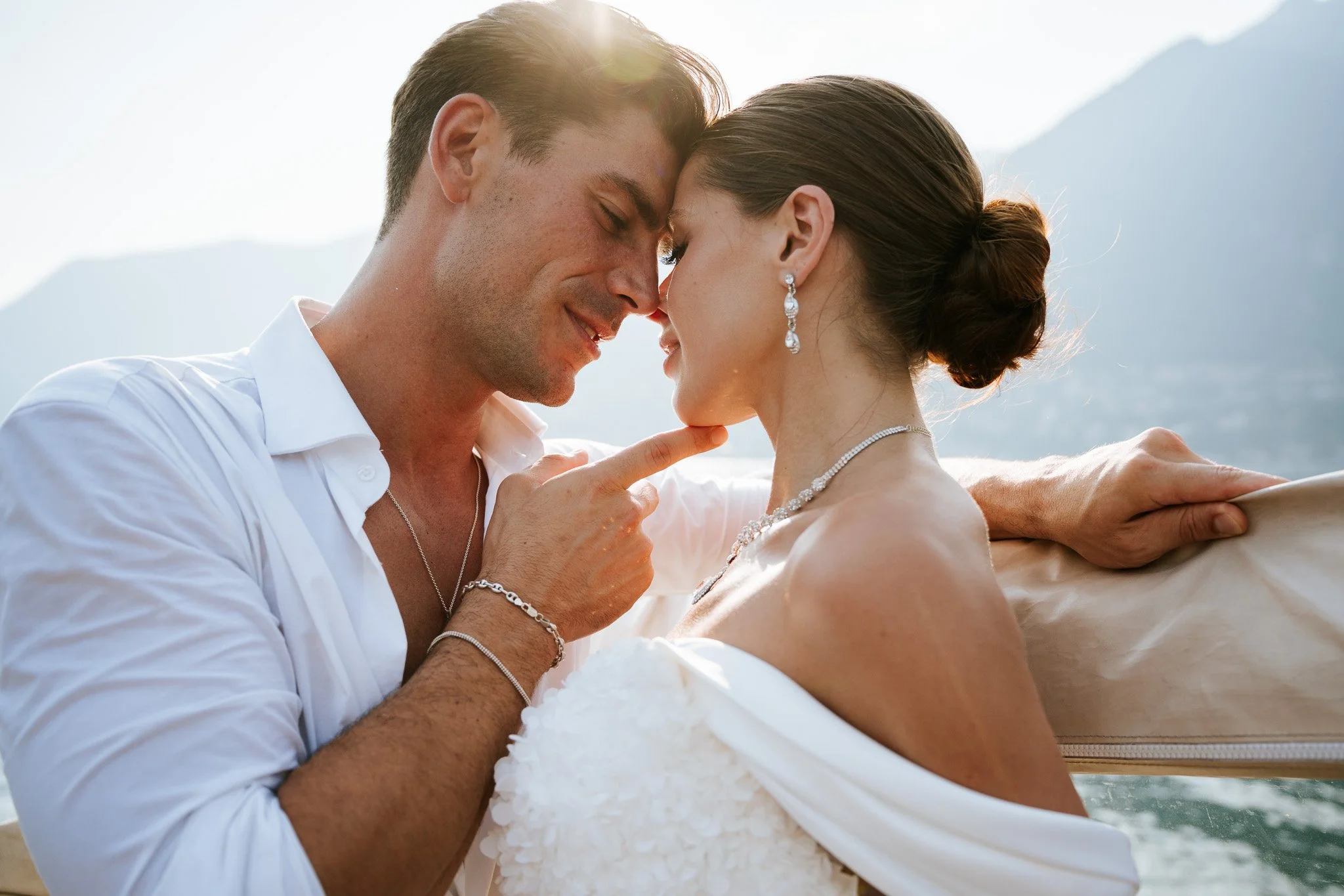 A couple touching foreheads and smiling, with mountains in the background, during daytime.