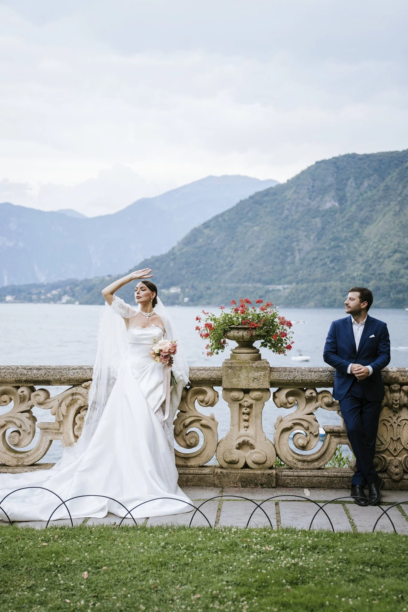 Bride and groom by the stone balustrade at Villa del Balbianello, Lake Como, with the lake and mountains behind them.