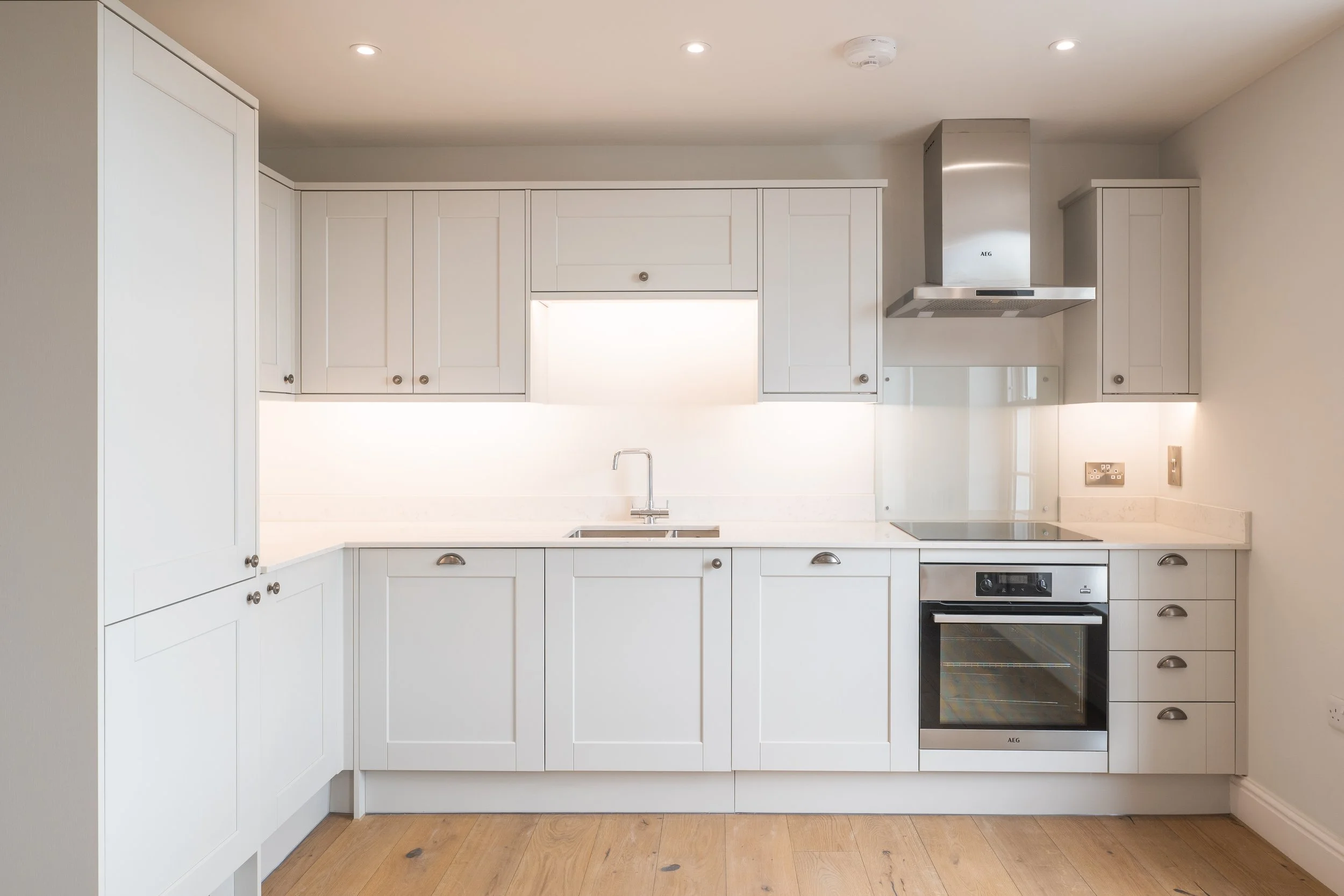 Modern white kitchen with cabinets, a stainless steel range hood, and a built-in oven.
