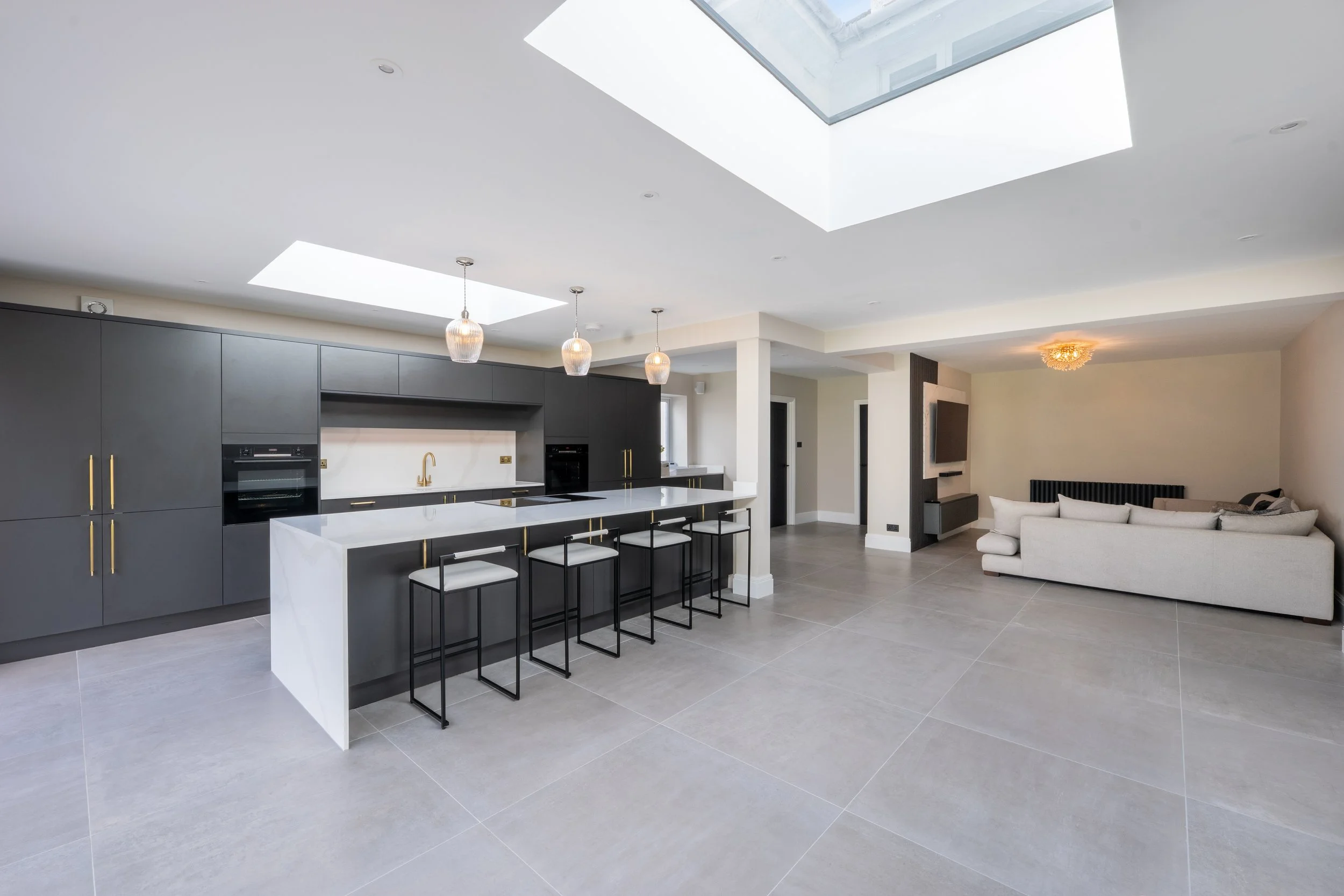 Modern open-concept kitchen and living space with gray cabinetry, white island, pendant lighting, large skylights, and a sectional sofa.