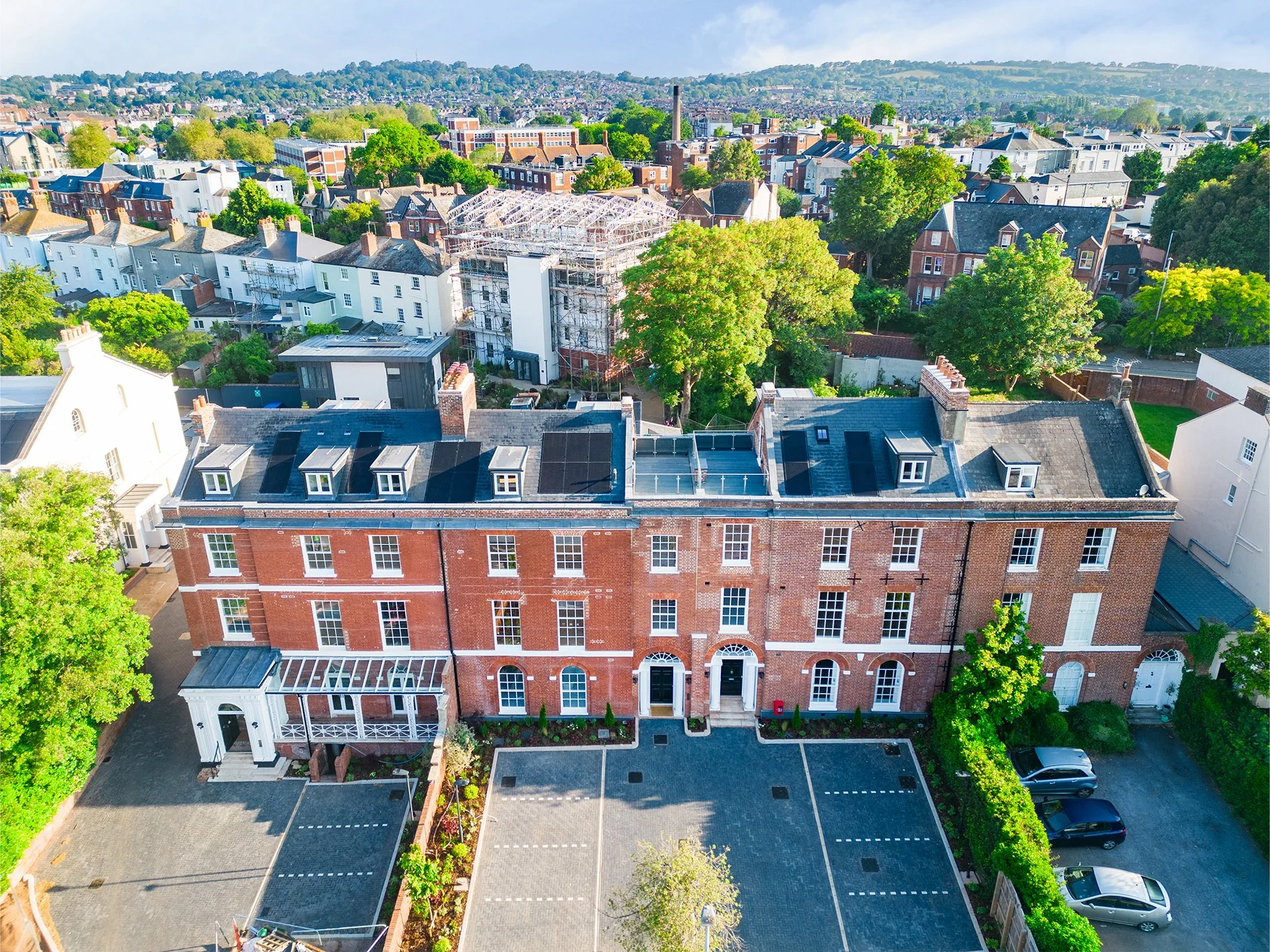 Aerial view of a city neighborhood with modern brick buildings, trees, and an under-construction building with scaffolding.