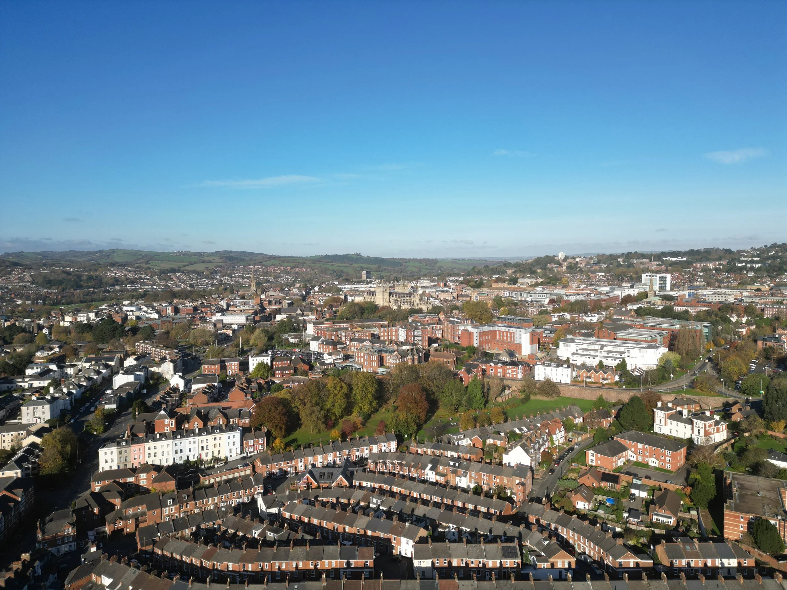 A cityscape with a mix of residential and commercial buildings under a clear blue sky, with green hills in the background.