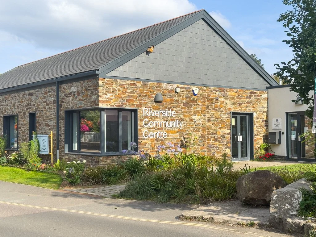 The Riverside Community Centre building with a stone and gray siding exterior, surrounded by a garden with colorful flowers, rocks, and shrubs, and clear skies overhead.