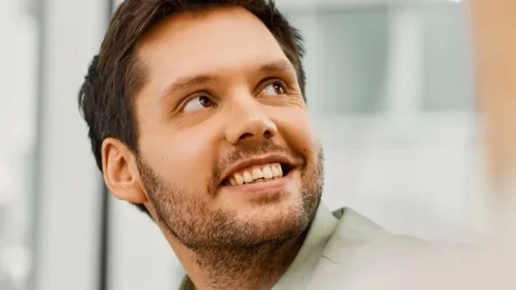 Close-up of a man with brown hair and a beard smiling and looking upward.