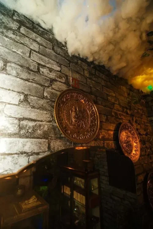 Golden ceremonial medallions on the stone wall beneath rolling mist in Witchcraft & Wizardry — Escape London Whitechapel