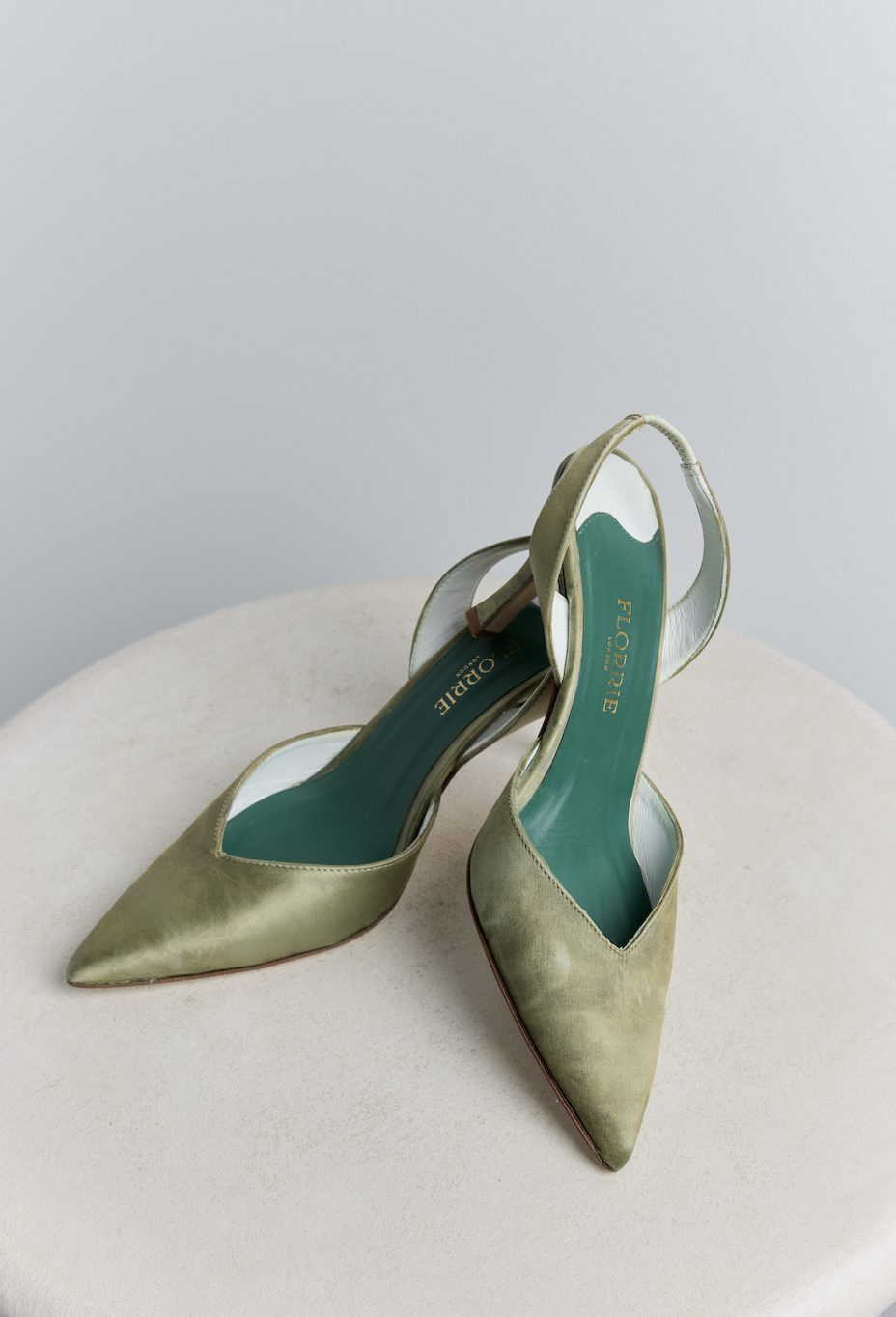 Green pointed-toe high heels with ankle straps placed on a light-colored textured surface.