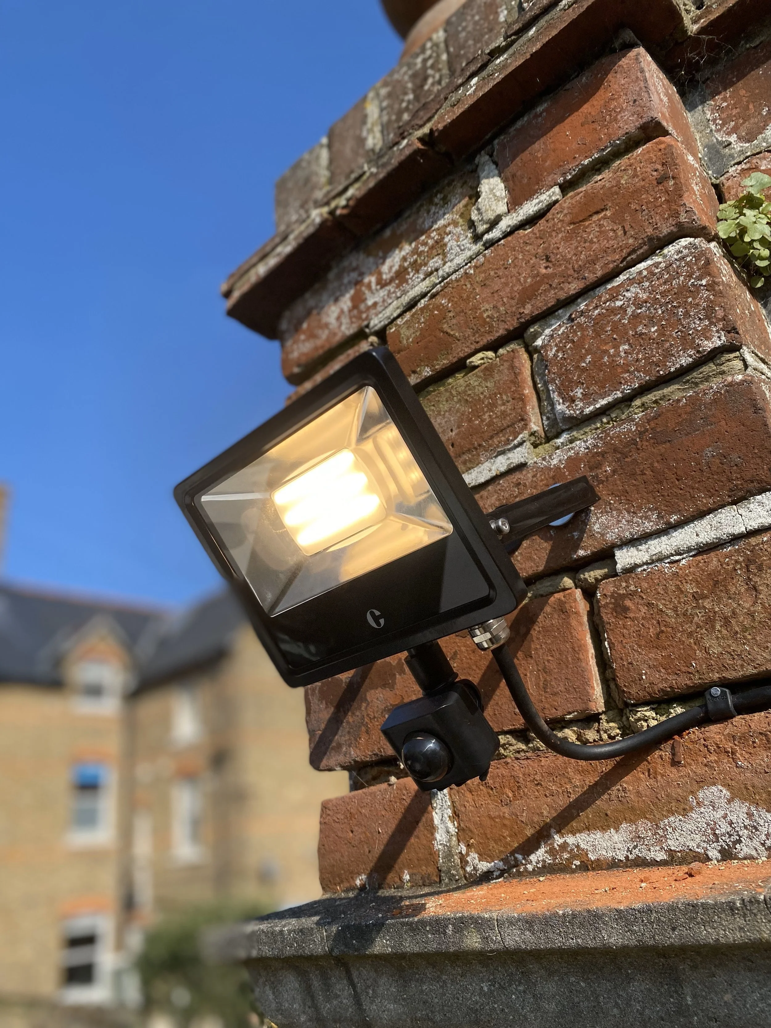 Close-up of a black outdoor light fixture mounted on a brick wall, with a blue sky in the background.