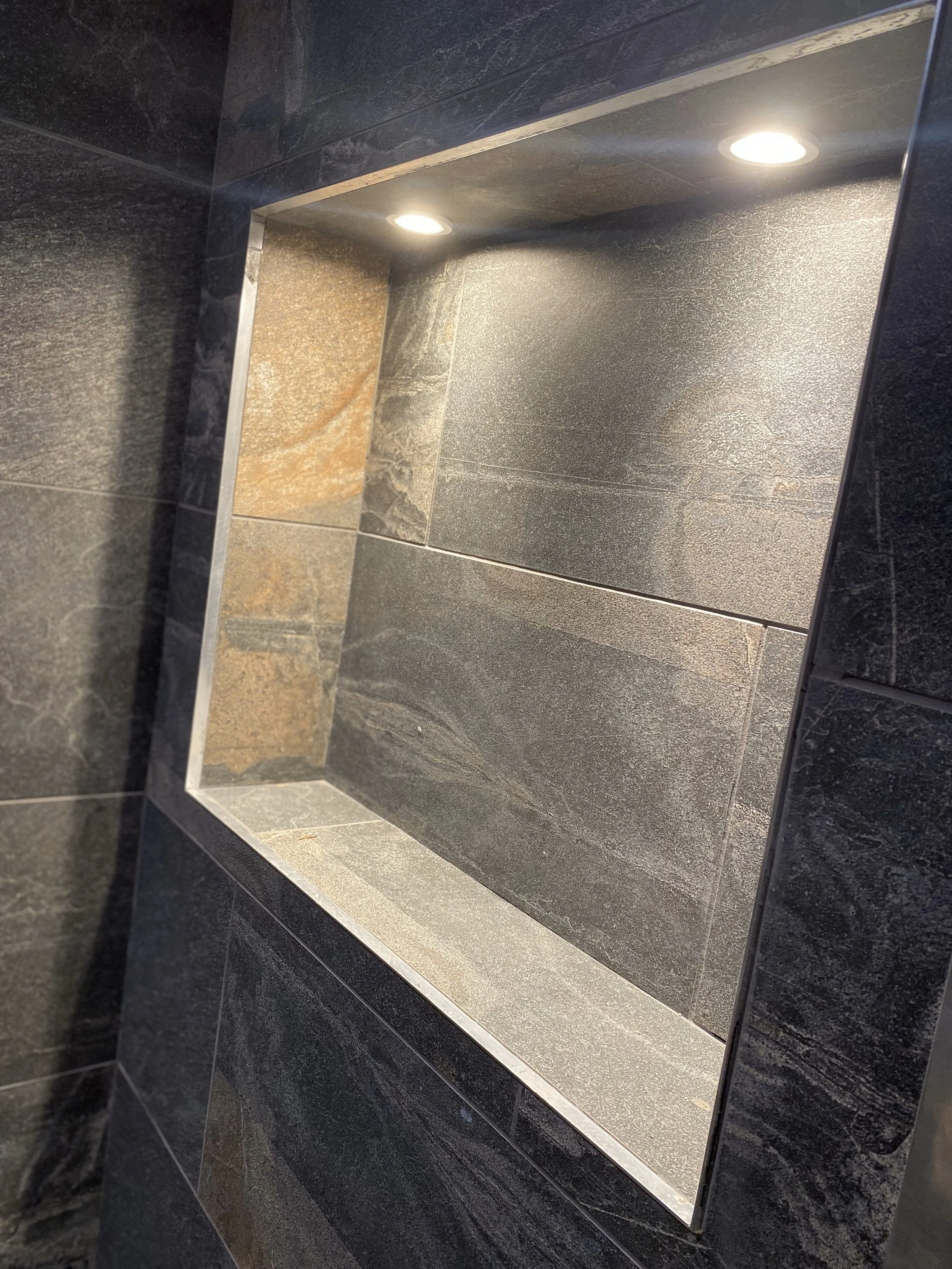 Close-up of a recessed light in a dark tiled wall and floor.