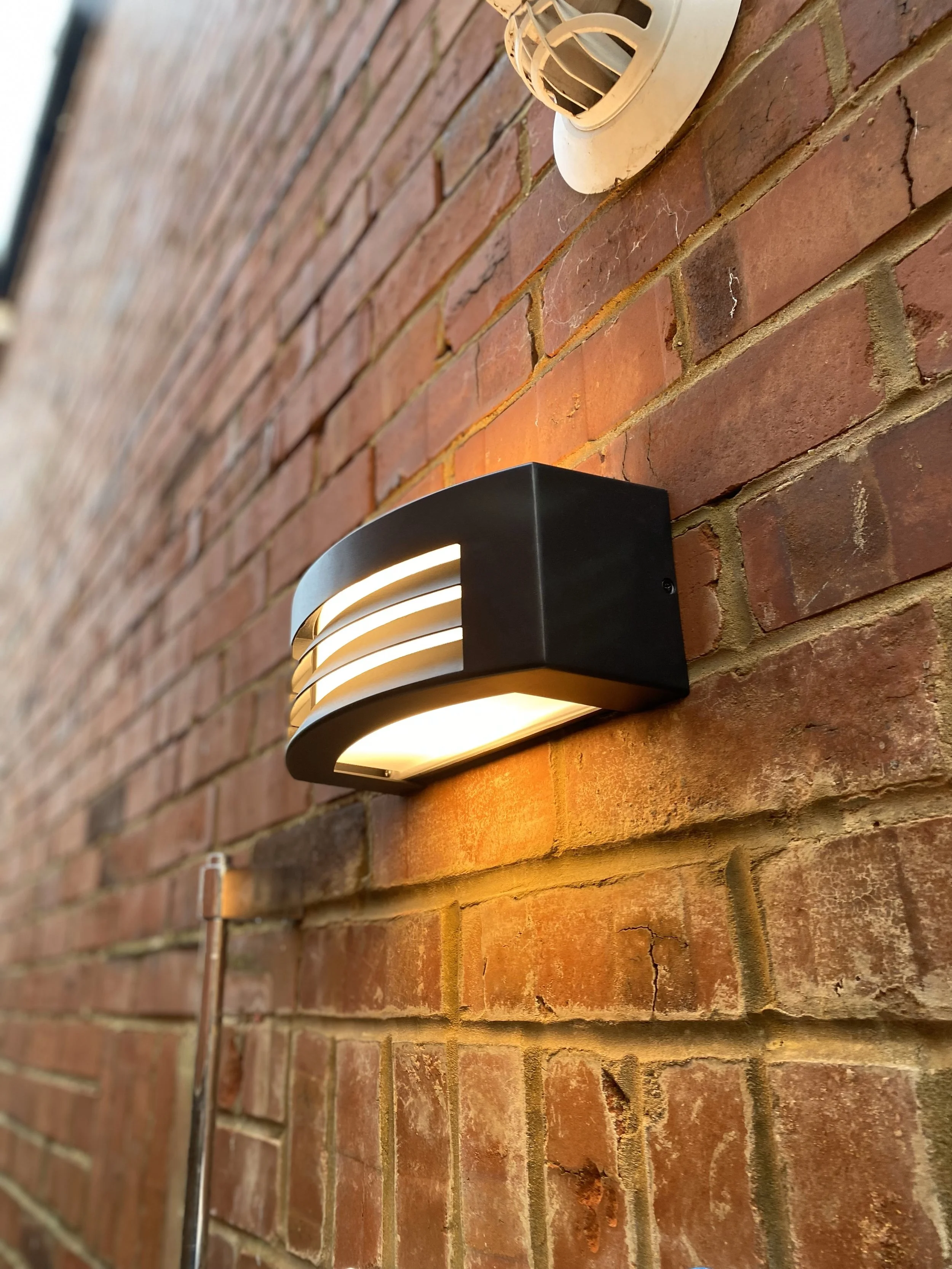 Close-up of a brick wall with a modern outdoor wall light fixture and an outdoor electrical conduit running along the wall.