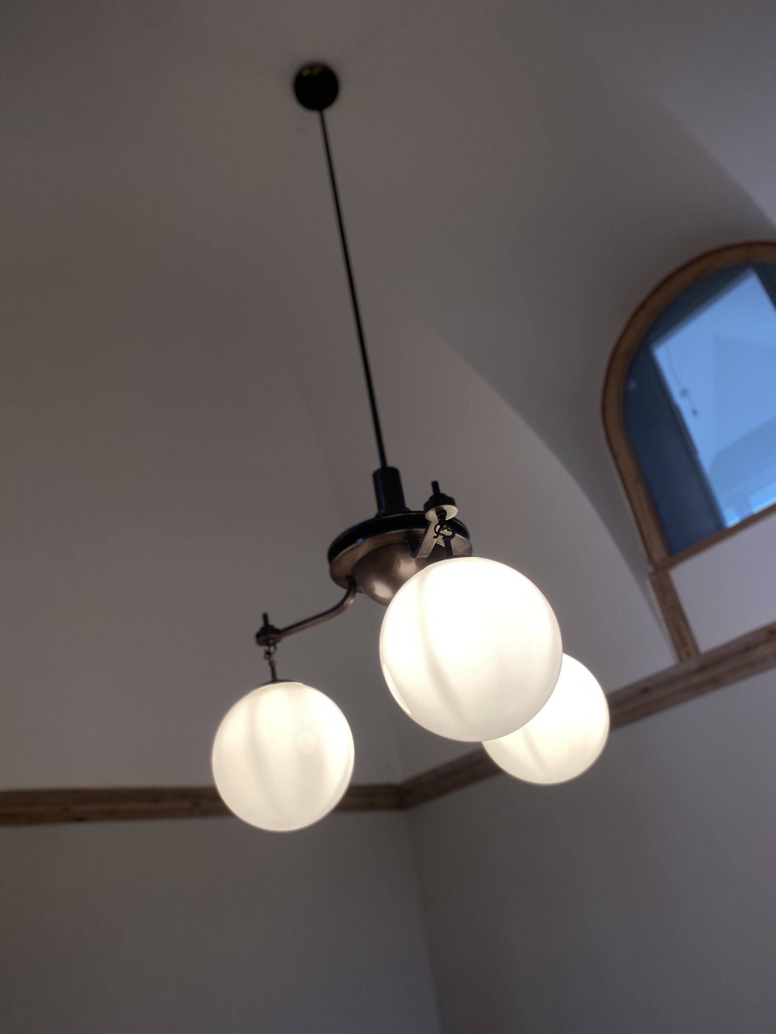 Ceiling light fixture with five spherical white glass globes hanging from black metal arms, placed in a room with a white ceiling and a skylight window.