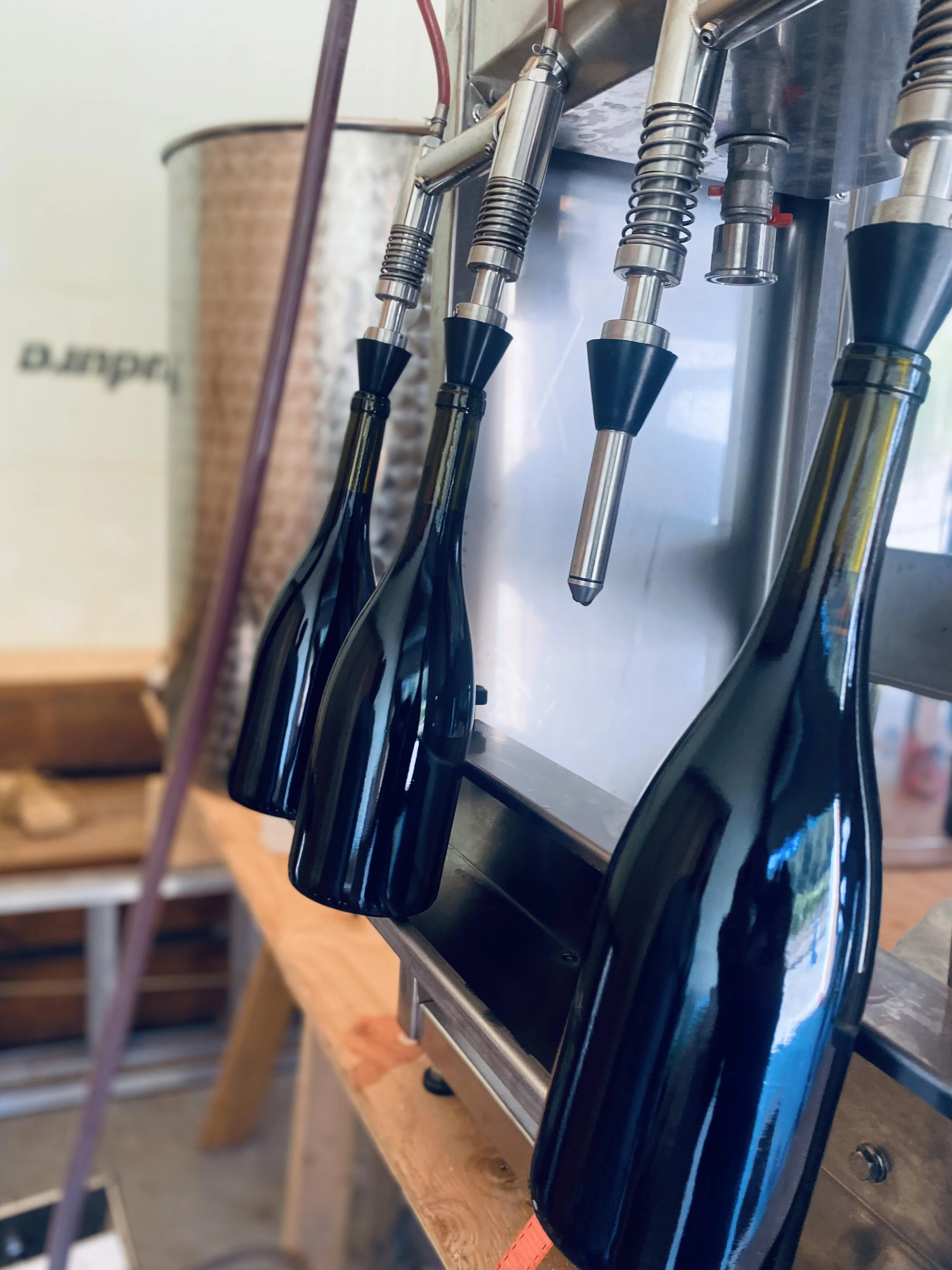 Four black soda bottles connected to a soda dispenser, stainless steel nozzles and springs, mounted on a metal surface.