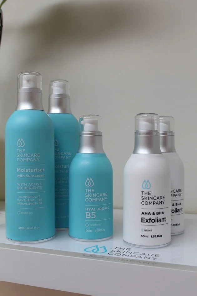 Several skincare products from The Skincare Company, including moisturizers, hyaluronic acid, and exfoliants, arranged on a shelf.