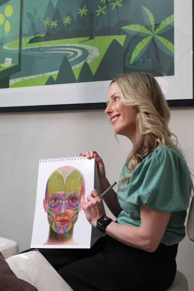 Woman smiling and holding a diagram of the human face with colorful acupuncture or pressure points.