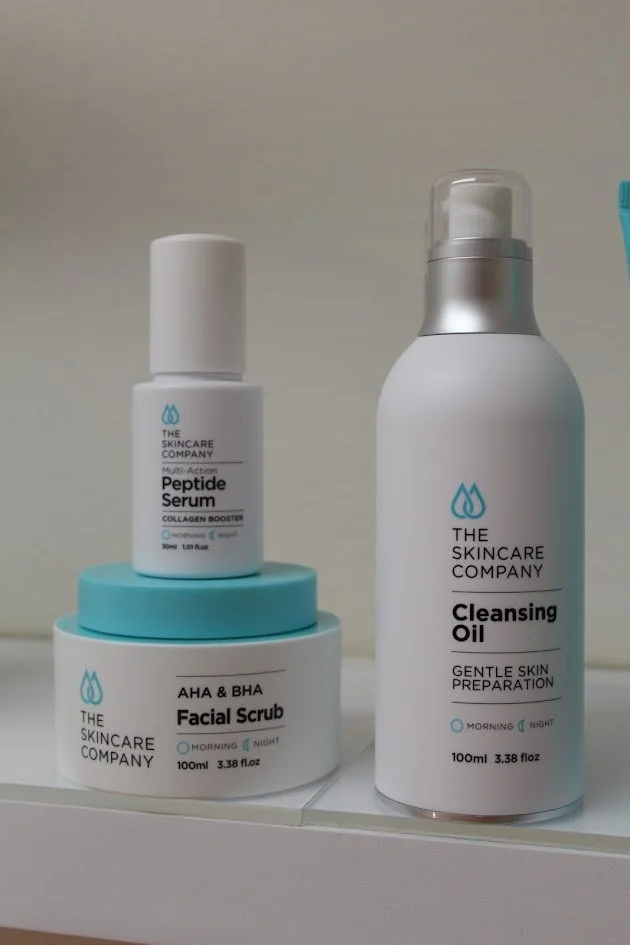 Skincare products including a facial scrub, peptide serum, and cleansing oil on a shelf.