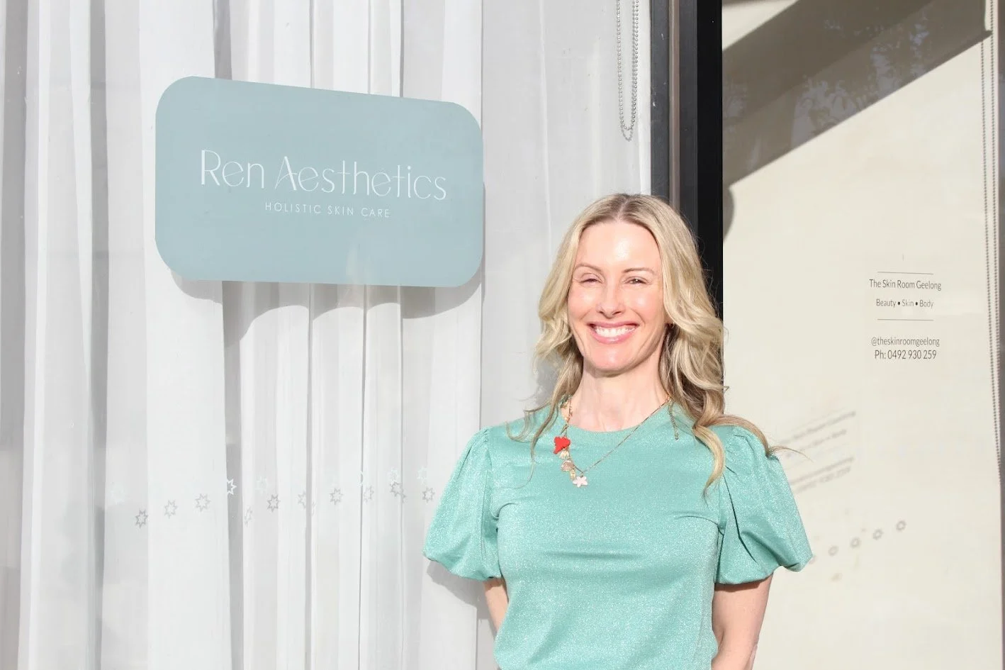 A woman with blonde hair smiling outside a skin care clinic called Ren Aesthetics.