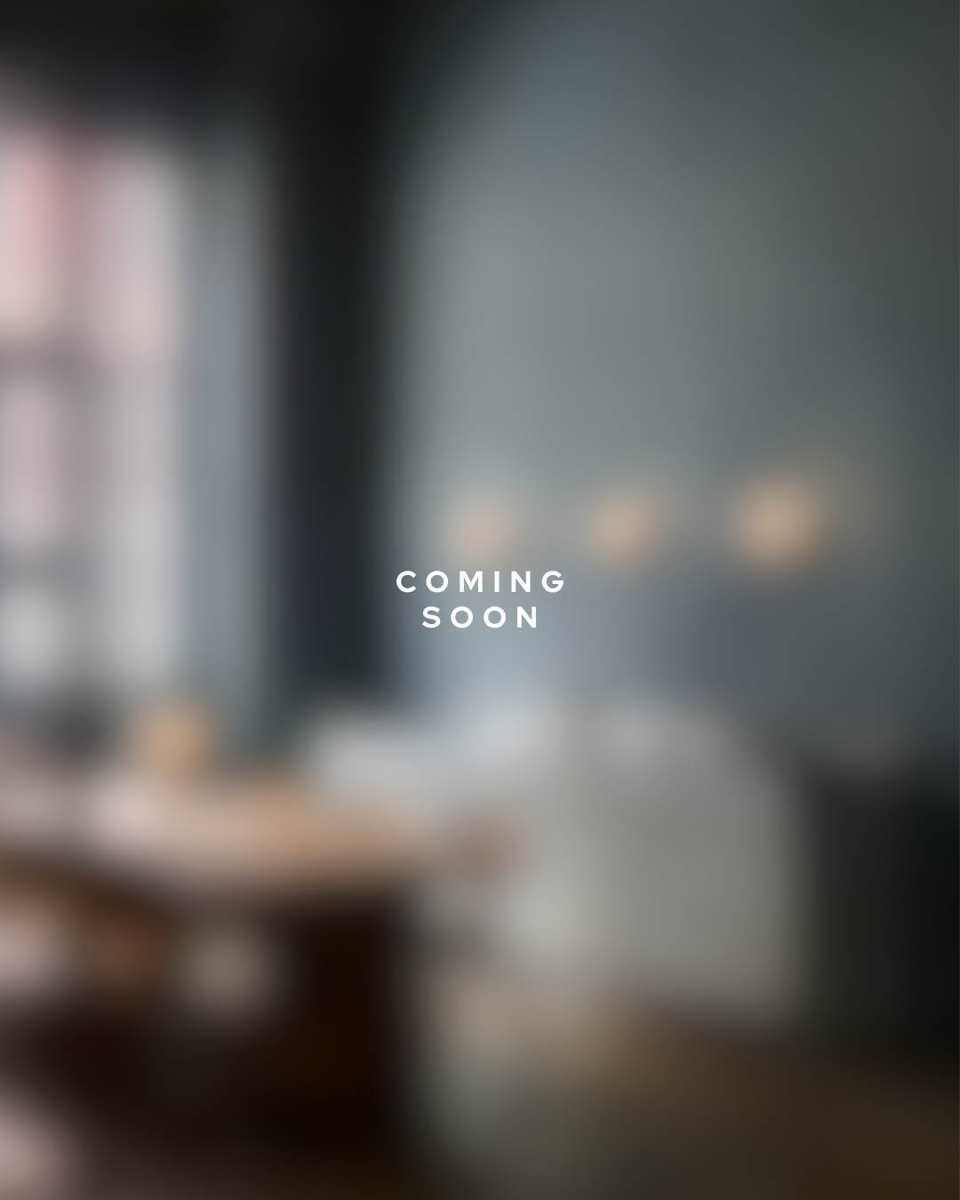 Verschwommenes Bild mit der Aufschrift 'Coming Soon' in der Mitte, Hintergrund möglicherweise ein modernes Wohnzimmer oder Büro.