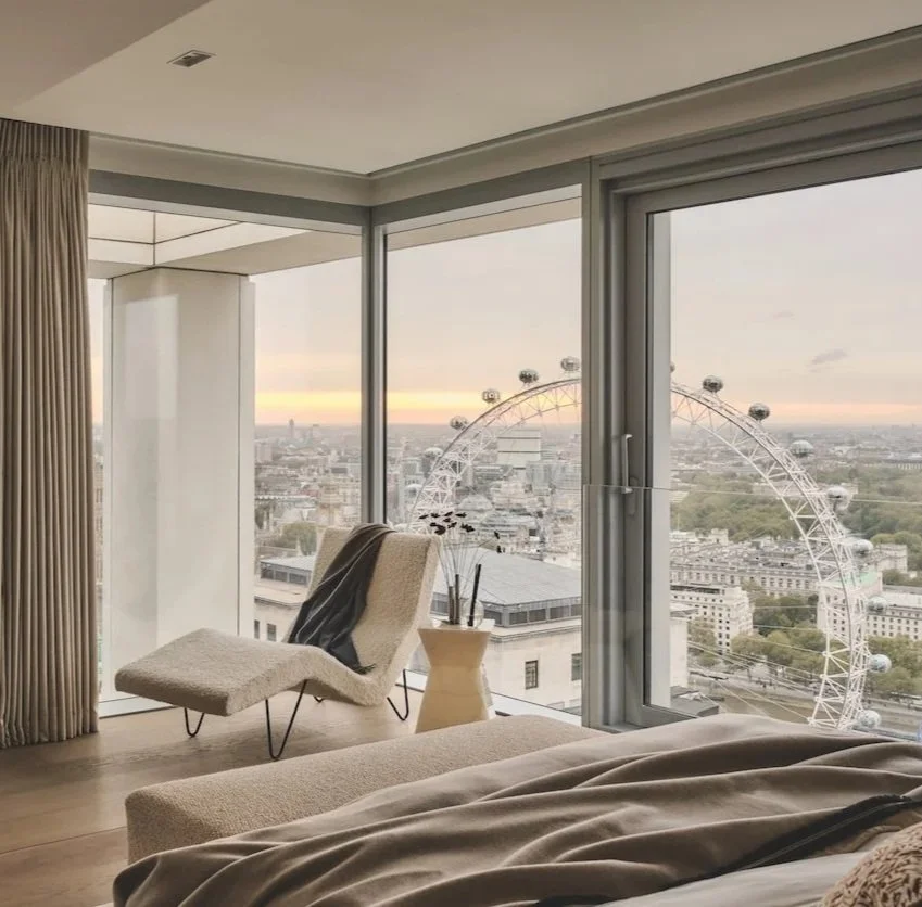 Luxury London apartment interior with floor-to-ceiling windows overlooking the London Eye and city skyline at sunset.