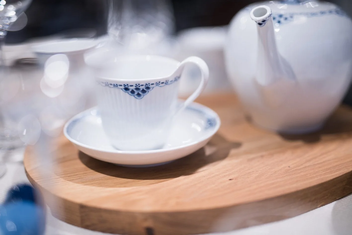 White porcelain teacup with blue pattern on a matching saucer, placed on a round wooden tray.