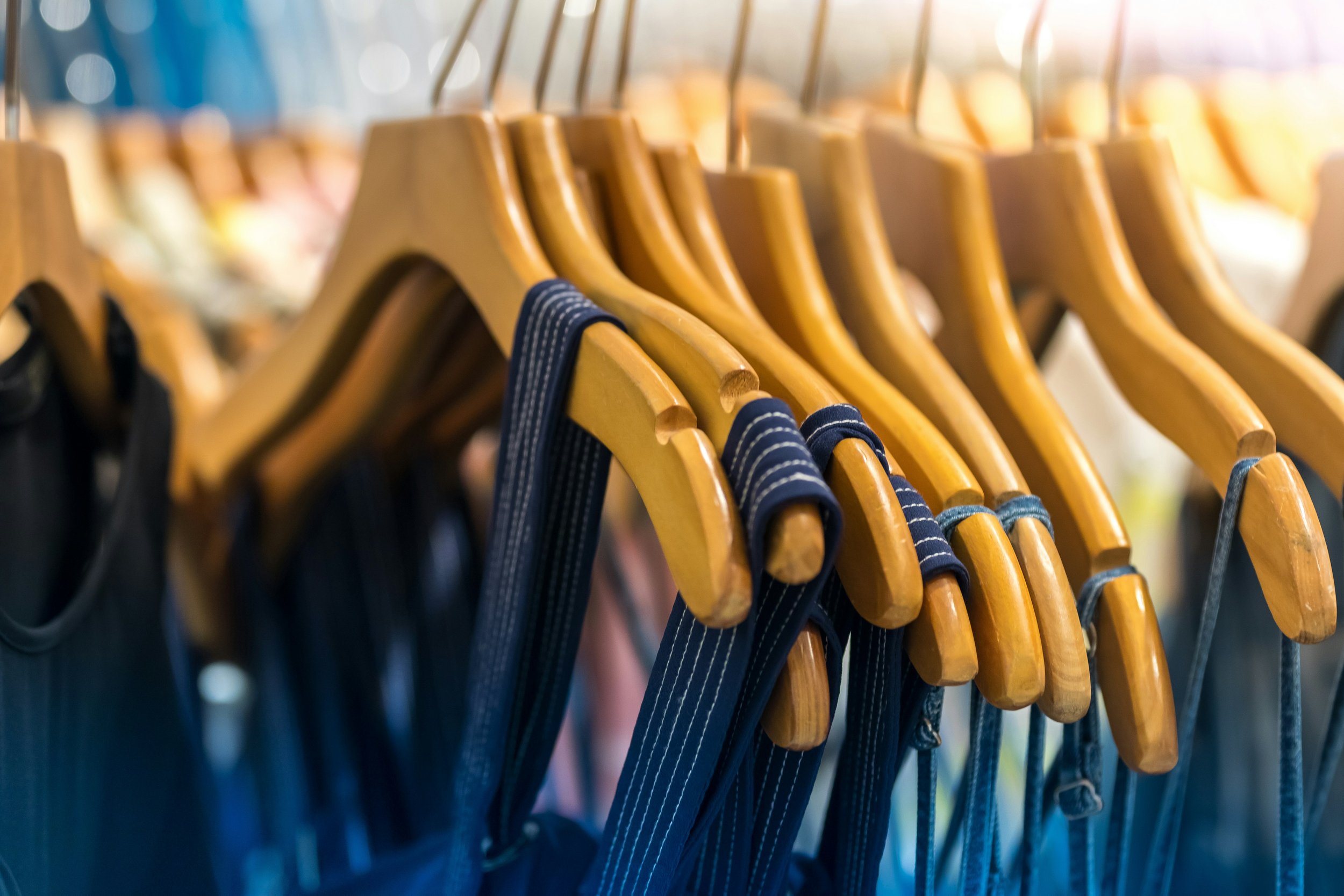 Wooden clothes hangers on a metal rack with various clothing items hanging, some with blue and striped patterns.
