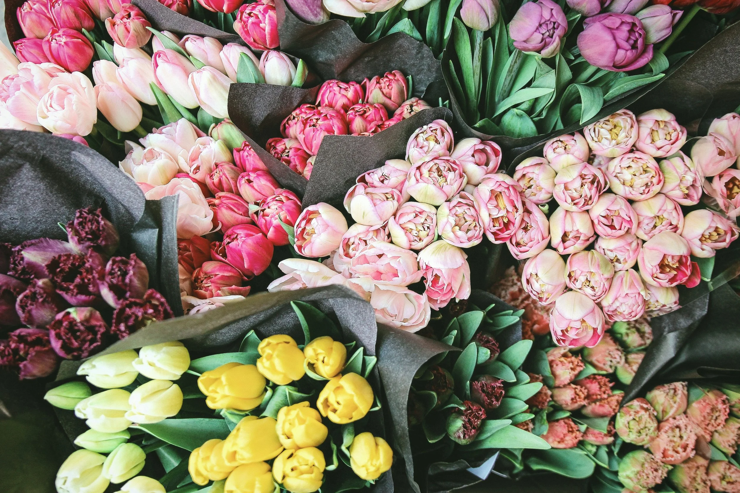 Various bouquets of pink, yellow, and purple tulips wrapped in black paper.