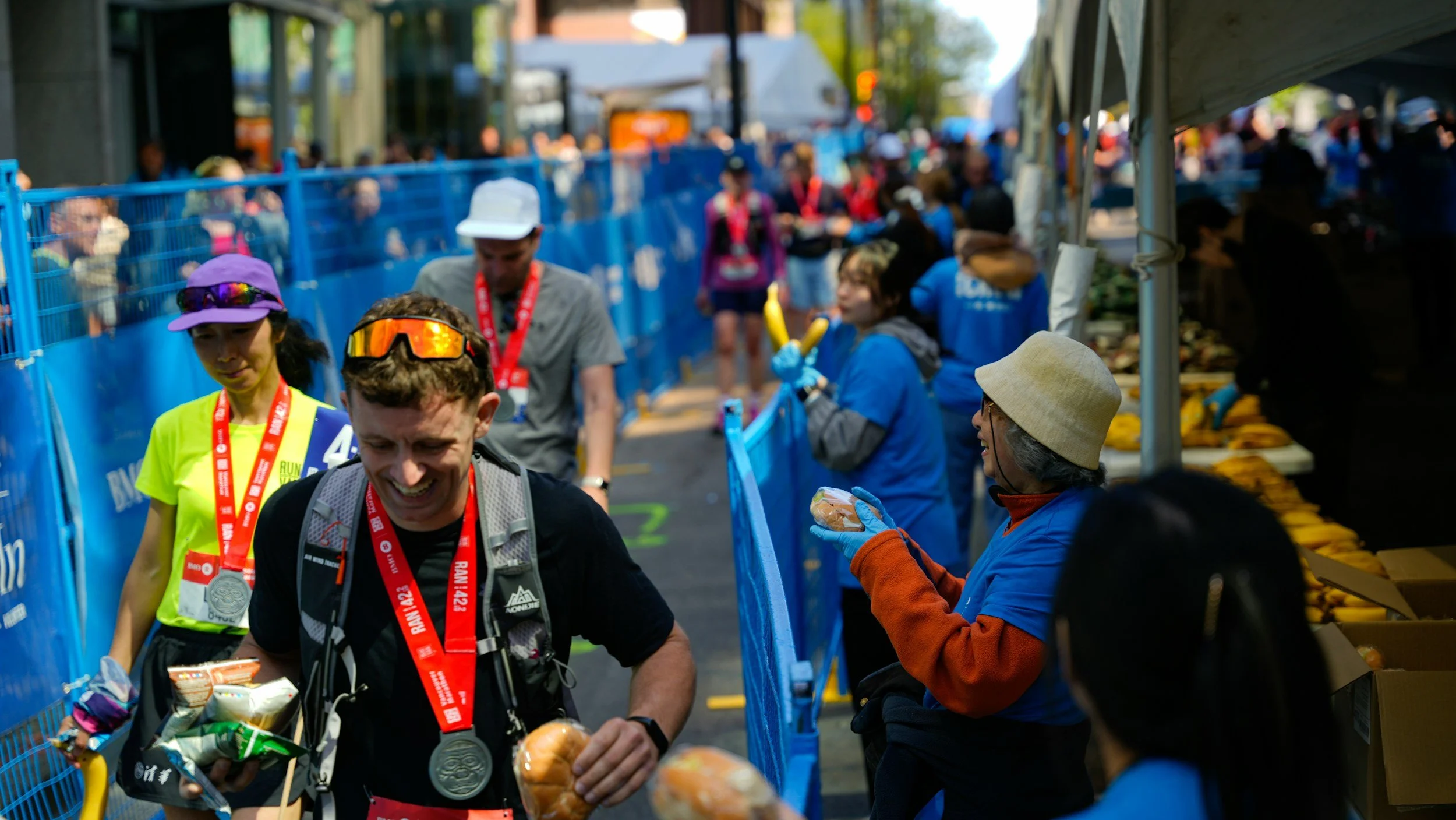Marathon runners crossing the finish line while volunteers distribute snacks and water.