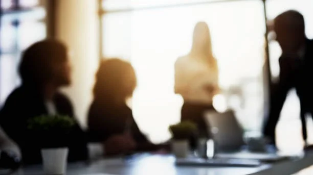 Silhouettes of five people in a business meeting, with sunlight streaming through a window in the background.