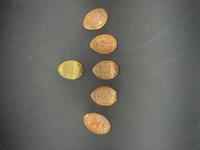 A collection of oval pressed pennies in copper, brass, and silver finishes
