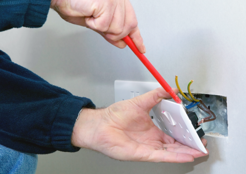 Person working on electrical outlet wiring with screwdriver.