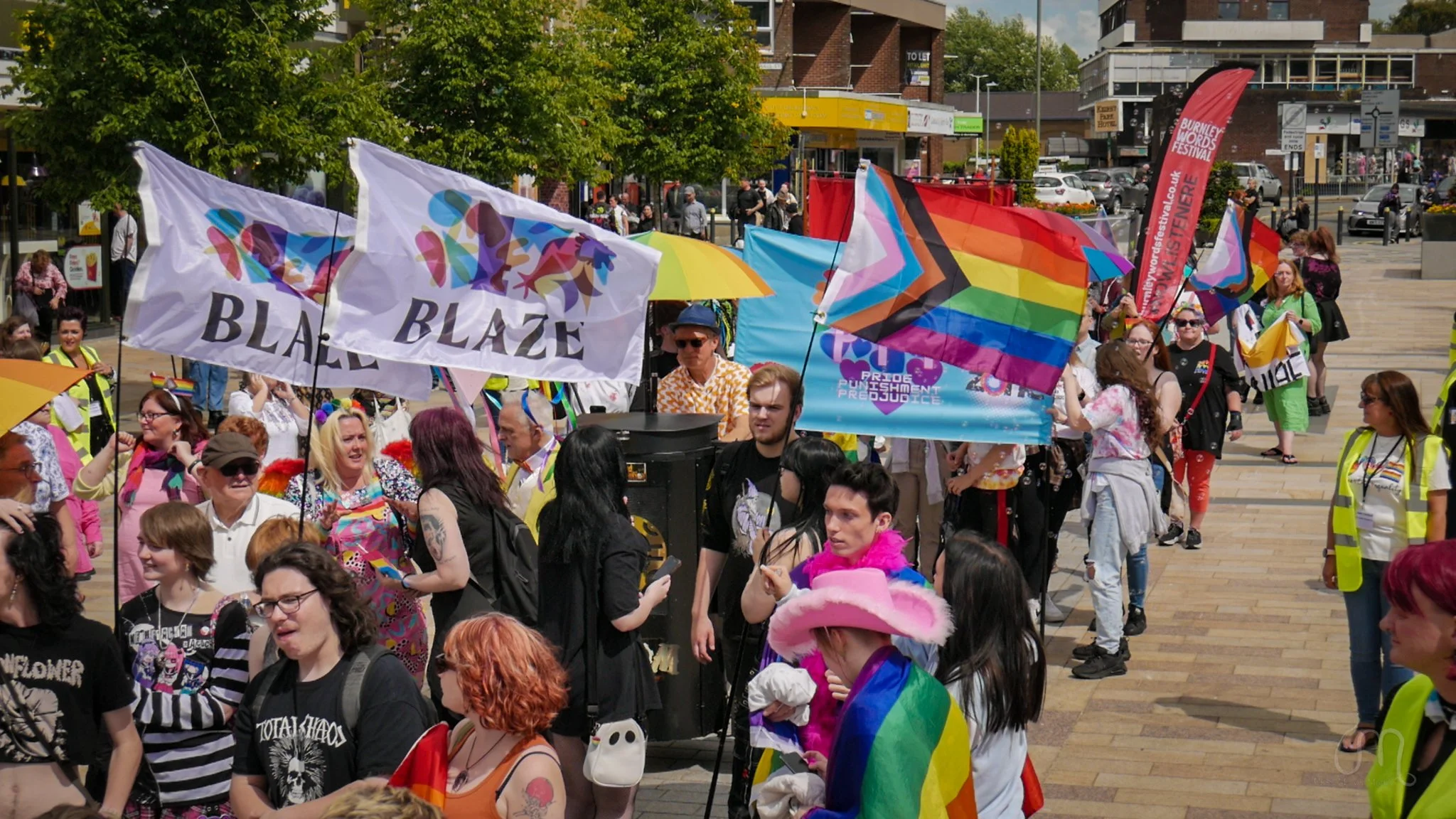 Crowd of people participating in a pride parade, holding rainbow flags, banners, and wearing colorful clothing.